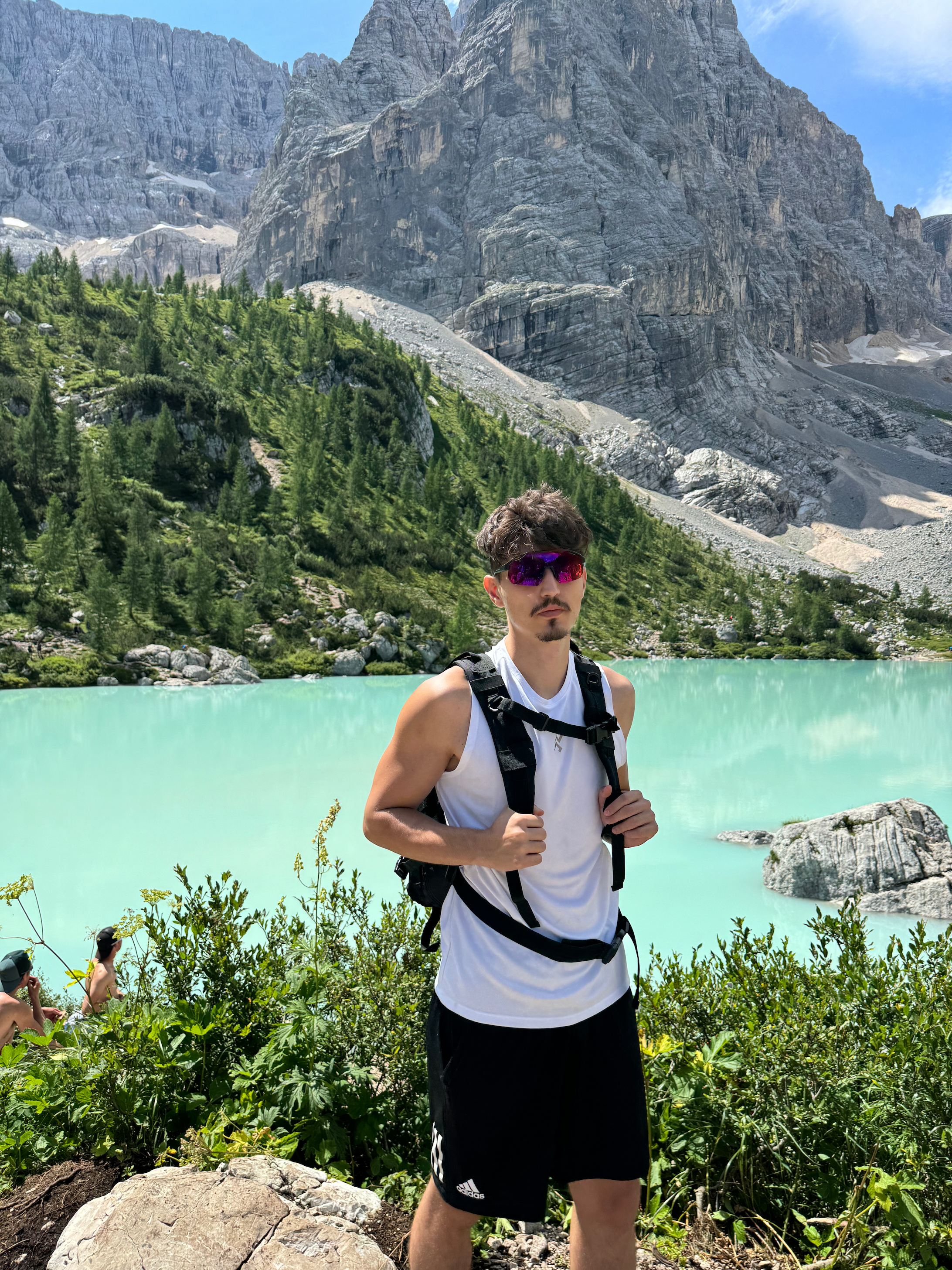 Hiker standing beside a turquoise alpine lake surrounded by towering mountains in the Italian Dolomites