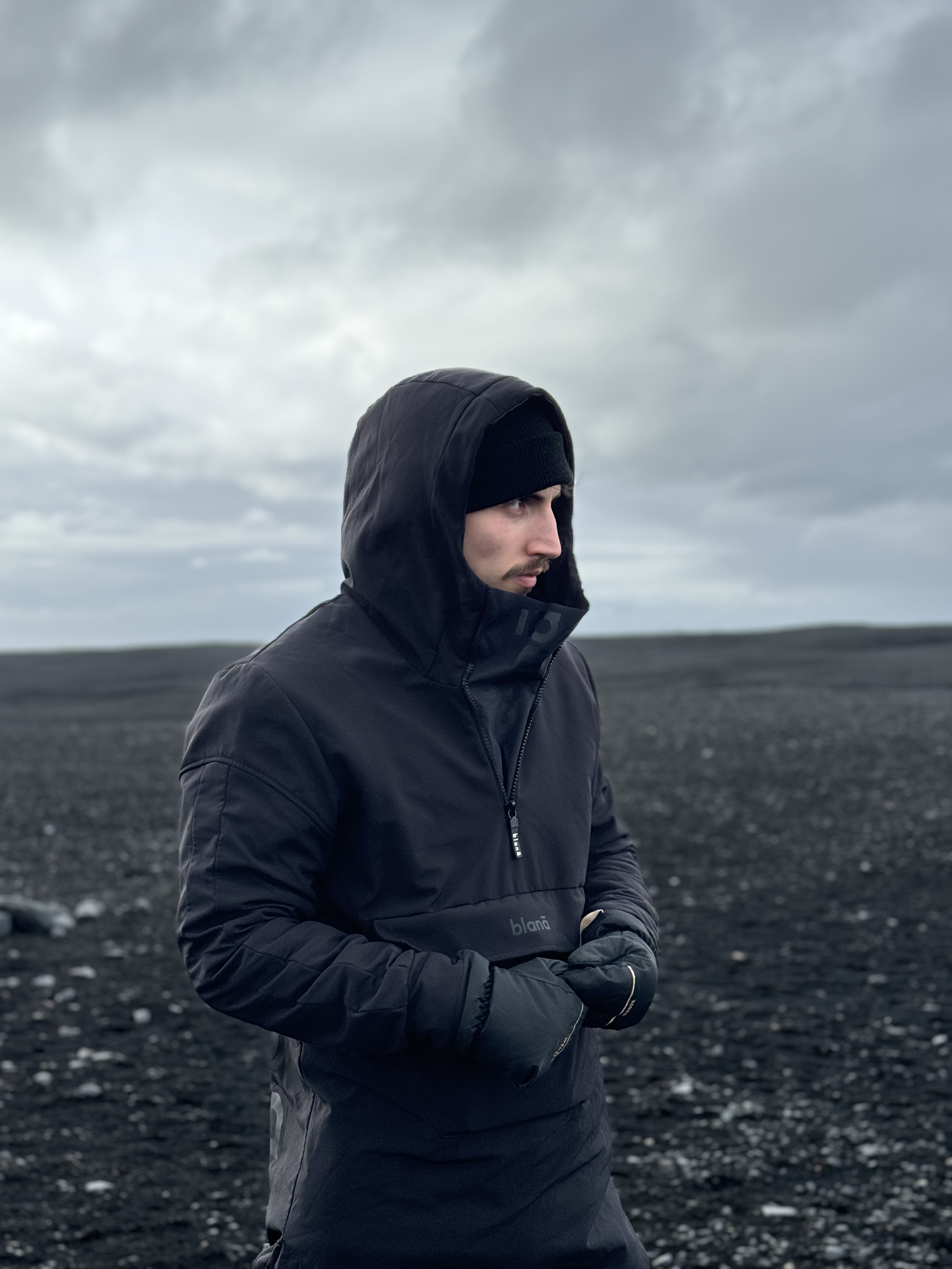 Traveler wearing a black hooded jacket against a dramatic, overcast landscape in Iceland